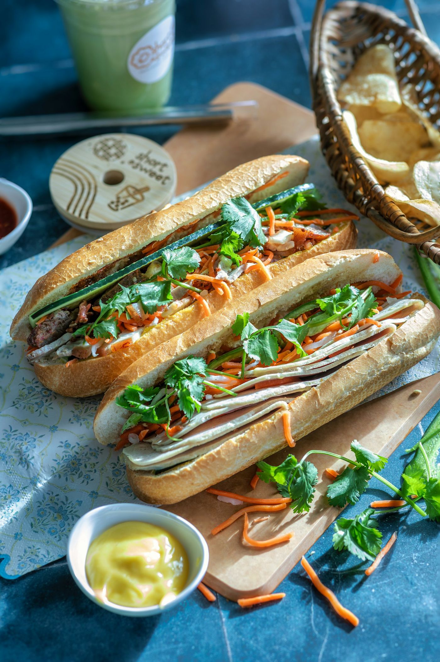 Two bánh mì on a wooden board with pickled carrot and herbs