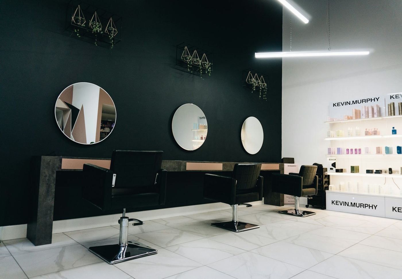 Salon chairs facing round mirrors on a dark wall